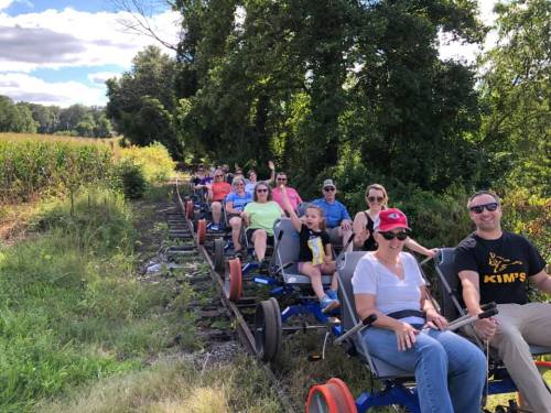 A group of people riding on a rail bike along a scenic path, surrounded by greenery and fields.