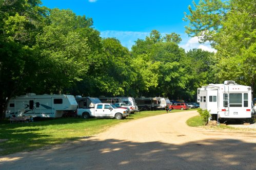 A gravel road lined with RVs and trees under a clear blue sky in a camping area.