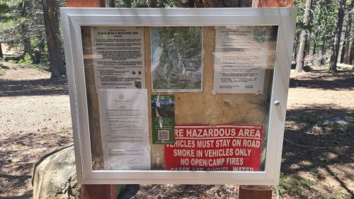 Information board in a forest area displaying safety notices, maps, and guidelines for visitors.