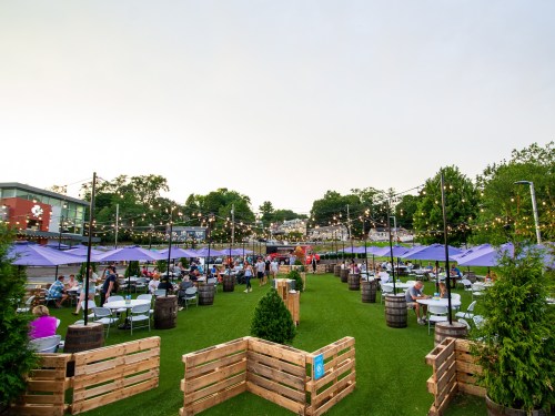 Outdoor dining area with string lights, tables, and umbrellas, filled with people enjoying a lively atmosphere.