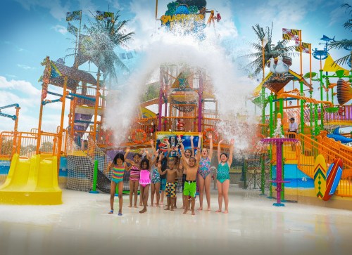 A group of children joyfully splashes water at a colorful water park, surrounded by slides and playful structures.
