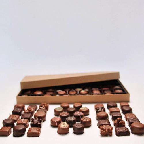 An assortment of chocolates displayed with an open box in the background, showcasing various shapes and textures.