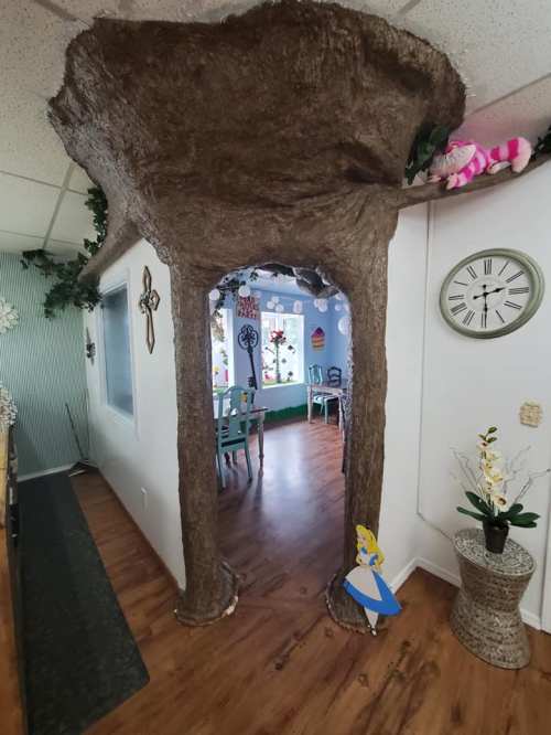 A whimsical archway resembling a tree trunk leads into a colorful room with decor and plants.