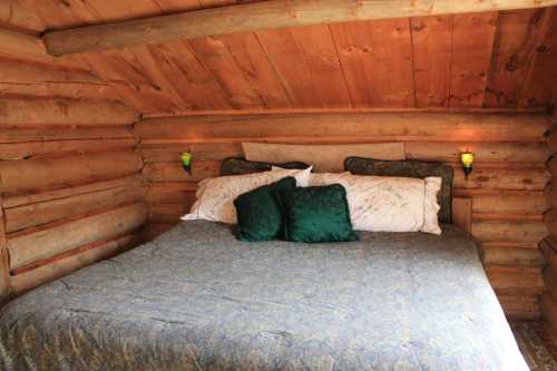 Cozy log cabin bedroom with a large bed, decorative pillows, and warm wooden walls. Soft lighting adds a welcoming touch.