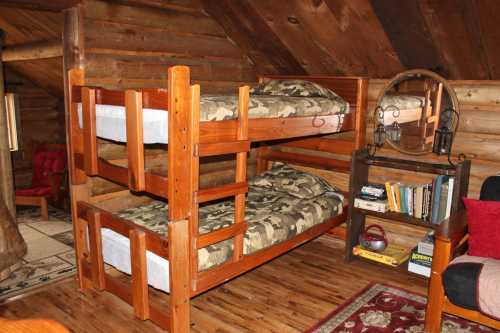 Cozy attic room with wooden bunk beds, camouflage bedding, and a small bookshelf beside a red chair.