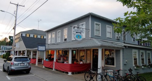 A quaint gray building with a sign for an ice cream parlor, surrounded by parked cars and bicycles.
