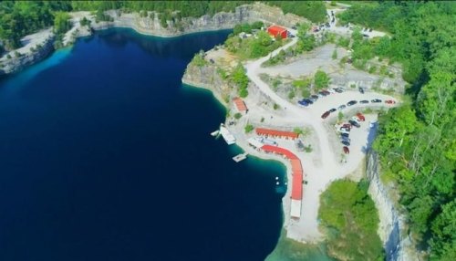 Aerial view of a blue lake surrounded by rocky cliffs, with a parking area and buildings along the shore.