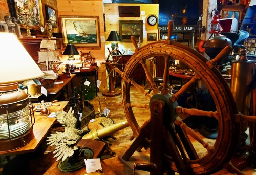 A cozy antique shop filled with various vintage items, including a ship's wheel, lamps, and nautical decor.
