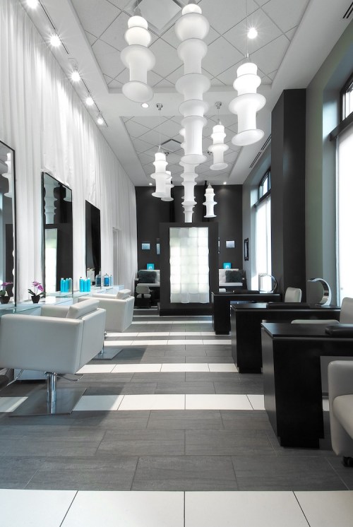 Modern salon interior with sleek white chairs, dark tables, and stylish pendant lights, featuring a bright, airy atmosphere.