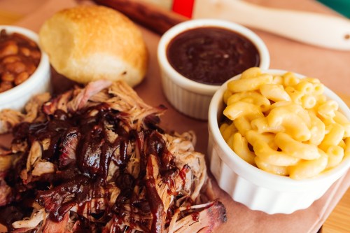 A plate featuring pulled pork with barbecue sauce, macaroni and cheese, baked beans, and a roll.