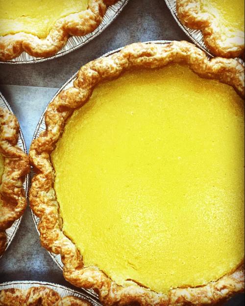 A close-up of several golden yellow pies with flaky, golden-brown crusts arranged on a surface.