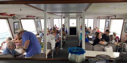 Interior of a boat with passengers seated at tables, chatting and enjoying the ride. Bright and spacious atmosphere.