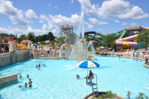 A vibrant water park scene with a large pool, water slides, and people enjoying the sunny day.
