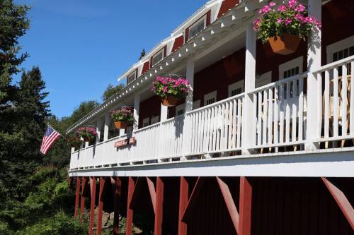 A red building with white trim and flower pots, featuring a porch and an American flag hanging from the side.
