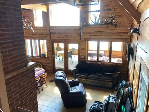 Cozy wooden cabin interior with a leather couch, dining area, and large windows letting in natural light.