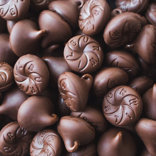 A close-up of numerous chocolate kisses, showcasing their shiny, smooth surfaces and iconic shape.