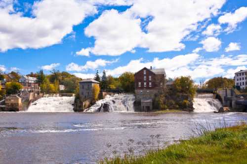 A scenic view of a waterfall with historic buildings alongside, under a blue sky with fluffy clouds.