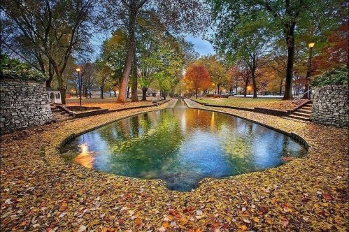 A serene park scene with a pond surrounded by colorful autumn leaves and trees, reflecting the vibrant fall colors.