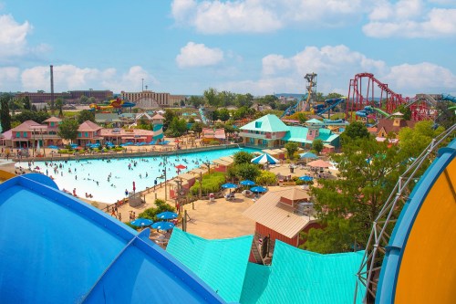A vibrant water park scene with pools, slides, and people enjoying the sunny day under blue skies.