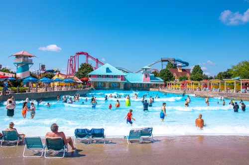 A vibrant water park scene with people enjoying a wave pool, colorful attractions, and roller coasters in the background.