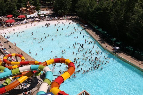 Aerial view of a crowded water park pool with colorful slides and many people enjoying the water on a sunny day.