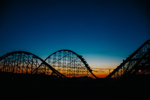 Silhouette of a roller coaster against a colorful sunset sky.