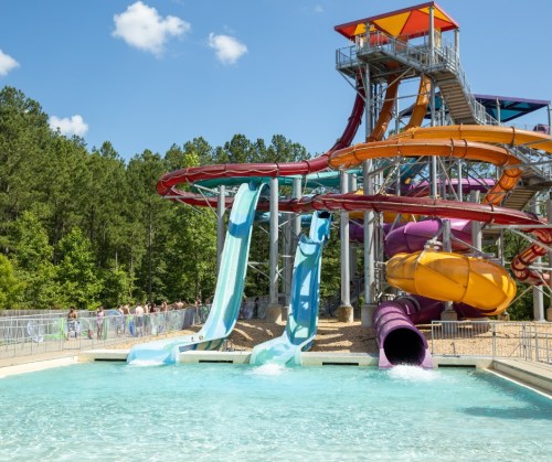 Colorful water slides at a water park, with a pool below and trees in the background under a clear blue sky.