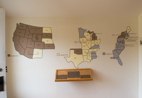 Wall-mounted map display showing various U.S. states in different shades, with a wooden plaque below.
