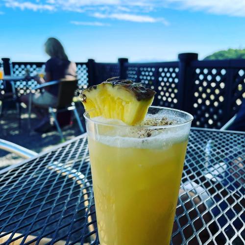 A refreshing pineapple drink on a table, with a scenic outdoor background and people enjoying their beverages.