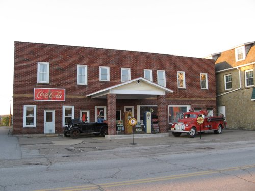 A brick building with a Coca-Cola sign, featuring an old car and a vintage fire truck parked outside.