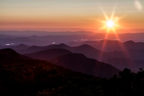 Sunrise over rolling mountains, casting a warm glow across the landscape with layers of hills in the background.