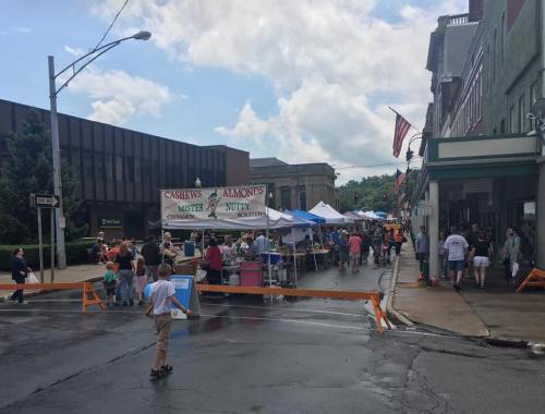 A bustling street fair with vendors, tents, and people enjoying the event under a partly cloudy sky.