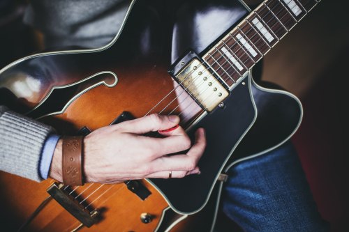 A close-up of a person's hand playing an electric guitar with a warm wooden finish.
