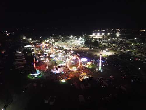 Aerial view of a vibrant night fair with colorful lights, rides, and a bustling crowd.