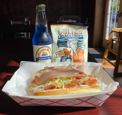 A sandwich with deli meats and lettuce, accompanied by a blue soda and a bag of buffalo ranch potato chips.