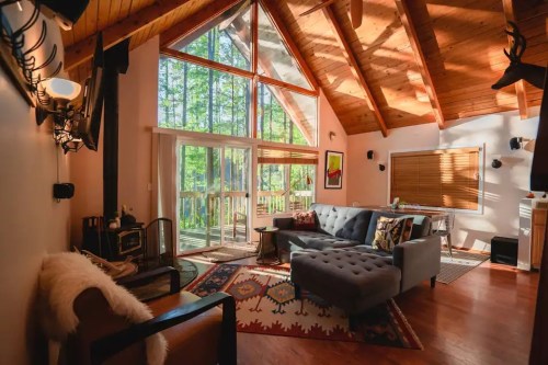 Cozy living room with a high wooden ceiling, large windows, a gray sofa, and a warm, inviting atmosphere.