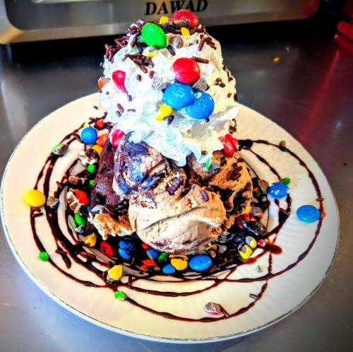 A decadent ice cream sundae topped with whipped cream, chocolate syrup, sprinkles, and colorful candies on a plate.
