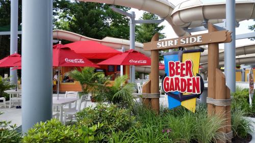 A colorful sign reading "Beer Garden" near red umbrellas and seating in a tropical outdoor setting.