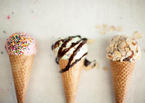 Three ice cream cones: one with pink sprinkles, one with mint and chocolate drizzle, and one with nuts.