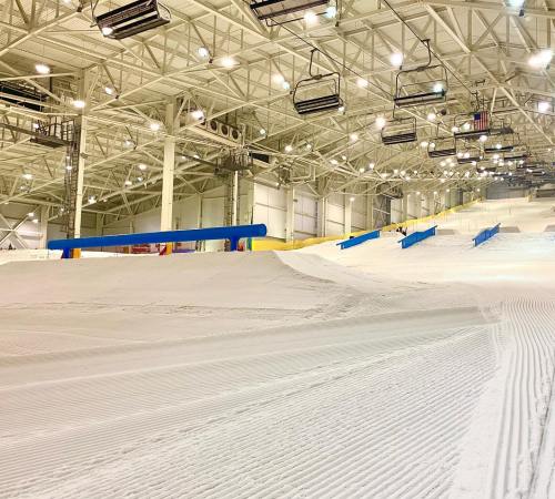 Indoor ski slope with groomed snow, ski lifts overhead, and a spacious, well-lit facility.
