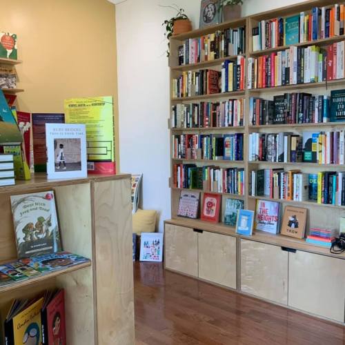 A cozy bookstore interior featuring wooden shelves filled with books and a display of children's books in the foreground.