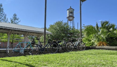 Bicycles parked on green grass with a water tower and trees in the background under a clear blue sky.
