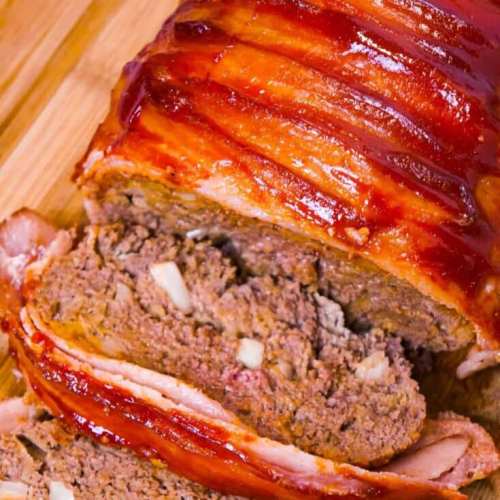 A close-up of sliced meatloaf with a glossy glaze, showcasing its juicy interior and crispy bacon topping.