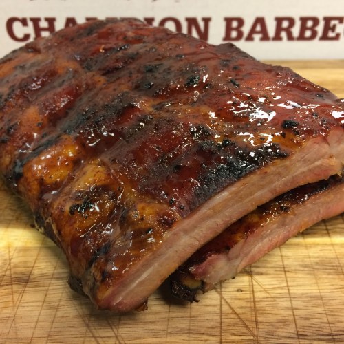 A close-up of a glazed, smoked rib rack resting on a wooden cutting board.