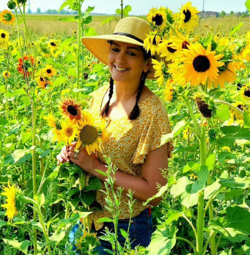 A woman in a straw hat smiles while holding sunflowers in a vibrant field of sunflowers.