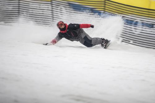 A snowboarder carves through fresh snow, creating a spray as they lean into a turn on a snowy slope.