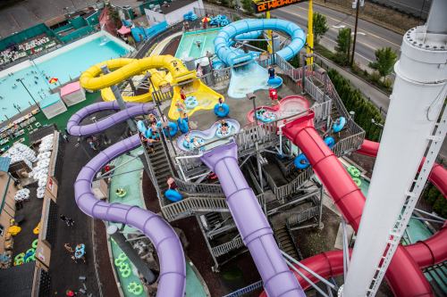 Aerial view of a colorful water park with multiple slides and a lazy river, surrounded by greenery and attractions.