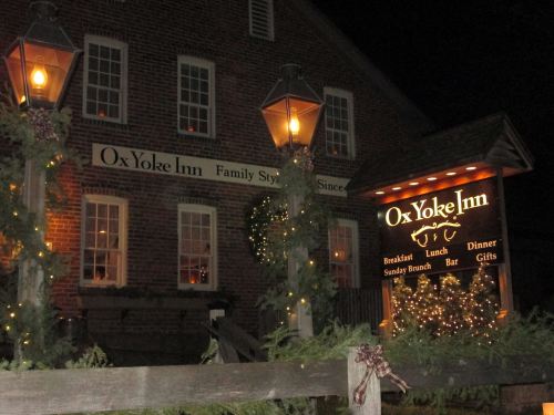 The Ox Yoke Inn, a brick building adorned with festive lights, features a sign for dining options and a warm, inviting atmosphere.