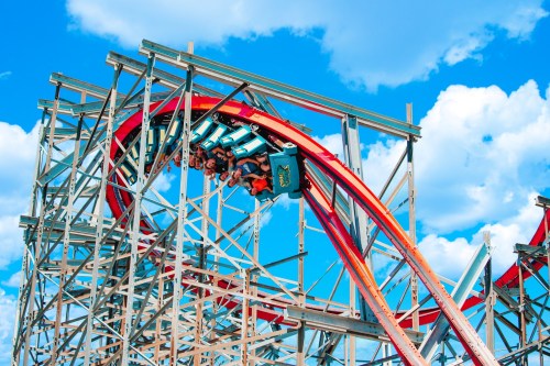 A roller coaster twists through a loop against a bright blue sky with fluffy clouds, riders enjoying the thrill.
