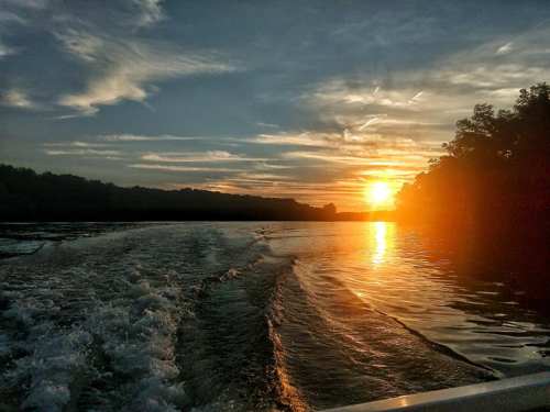 A serene sunset over a river, with rippling water and silhouettes of trees along the shore.